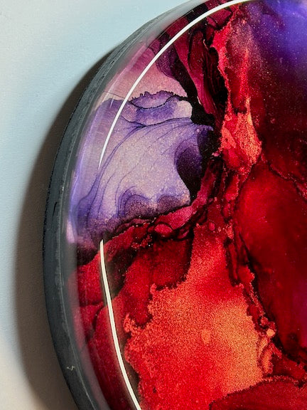 Planes of Passion,’ an abstract wall painting topped with resin, featuring shades of red, violet and maroon. Copper ink runs in striations throughout.