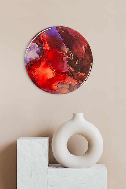Round abstract painting with red and purple hues on a beige wall, accompanied by a white vase. Symbolism art of passion, transformation and rising from adversity - an original artwork piece that would fit perfectly into modern homes and apartments - or a bedroom, living room, loft of hall.