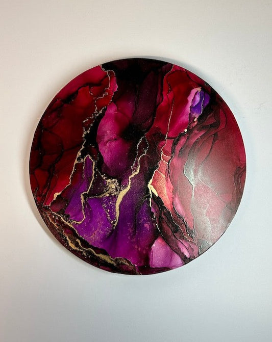 Fuelling the divine feminine through willpower. Rebellion, a circular abstract wall art painting featuring waves and ripples with tones of dark reds and violet. Metallic brass ink fractures overlay the painting. Matt finish. Interior art by Inkandescent Arts. Original red and purple abstract wall art expression. Original red abstract  round.