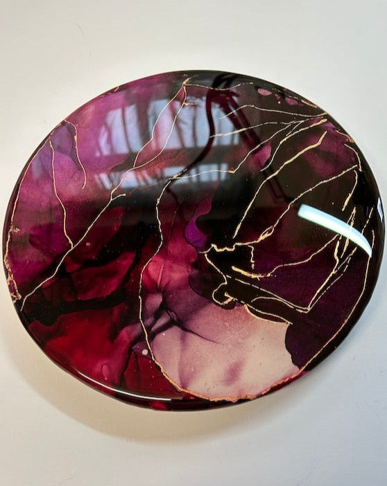 An original, fluid ink circle of bold, deep, heated colours of red and purple integration. Plates part, revealing lighter tones. Metallic veins holding fragments. With themes of life-force and the divine feminine by Inkandescent Arts. Original resin red abstract wall art expression. RESIN  ABSTRACT WALL ART EXPRESSION.