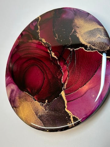 Depths of fire is a portrayal of self acceptance. An expression of the life-force and energy that resides inside us, it is an elegant, original abstract painting featuring deep reds, hints of aubergine, slips of hot pink and gold ink. Topped with resin, fractures and dark spirals intersect across the span of this 8” circular wall art by Inkandescent Arts. Original  round red resin abstract wall art expression.