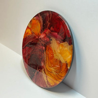 Interior, abstract, wall art. Created in fluid ink, its deep tones of red and orange fill the entirety of the circle.  Topped with resin, gold details highlight the flow of ripples whilst black edging accentuates the rich tones of this original artwork. An expression of auras by Inkandescent Arts.