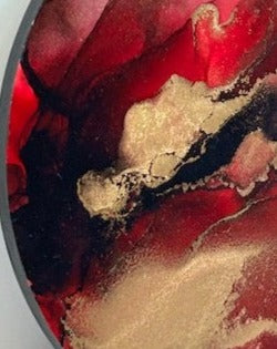 A close up of ‘Instinct,’ an original abstract fluid painting full of fiery, bold blends of deep red and black. Metallic brass striations erupt throughout. By Inkandescent Arts. Original round red abstract wall art expression.  RED ABSTRACT RED AND GOLD WALL ART.