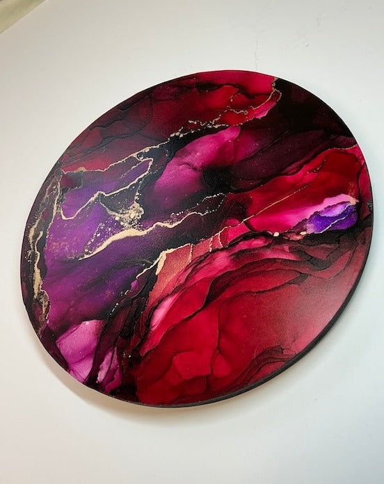 Rebellion - An interior abstract wall art painting where dark red and violet collide and flow, waves and ripples creating fissure-like depths atop the hues. Metallic brass tangles along the fissures. Aura expressed original fluid painting. Finish: matt. Size: 10" circular artwork by Inkandescent Arts.