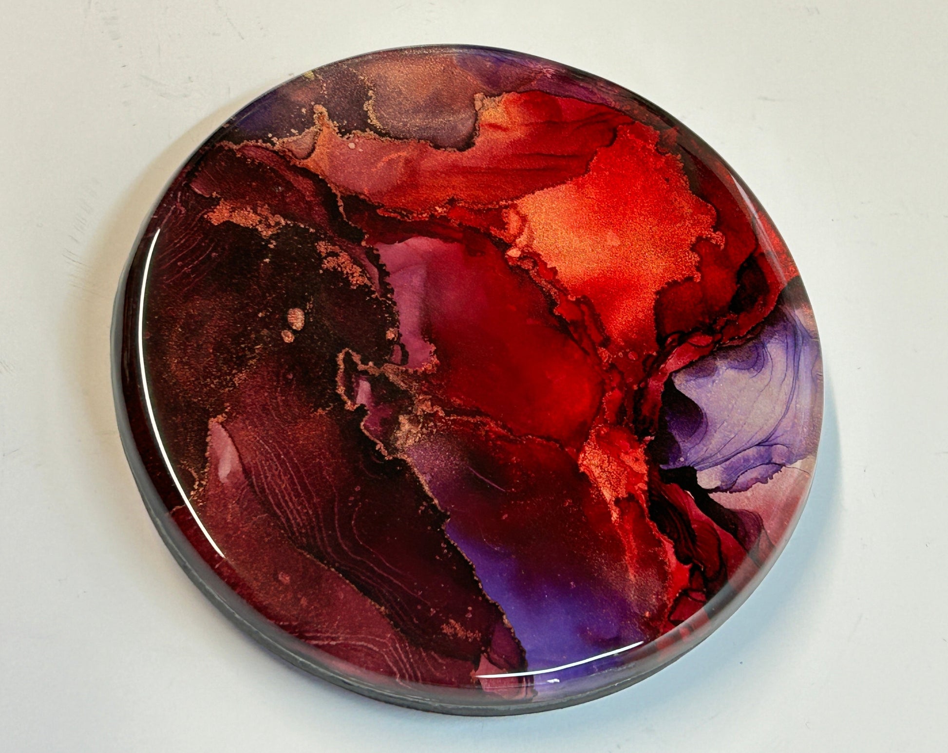 Based on auras, Planes Of Passion delves into the light within and inner fire.  An abstract wall painting topped with resin, featuring shades of red, violet and maroon. Copper ink runs in striations throughout.