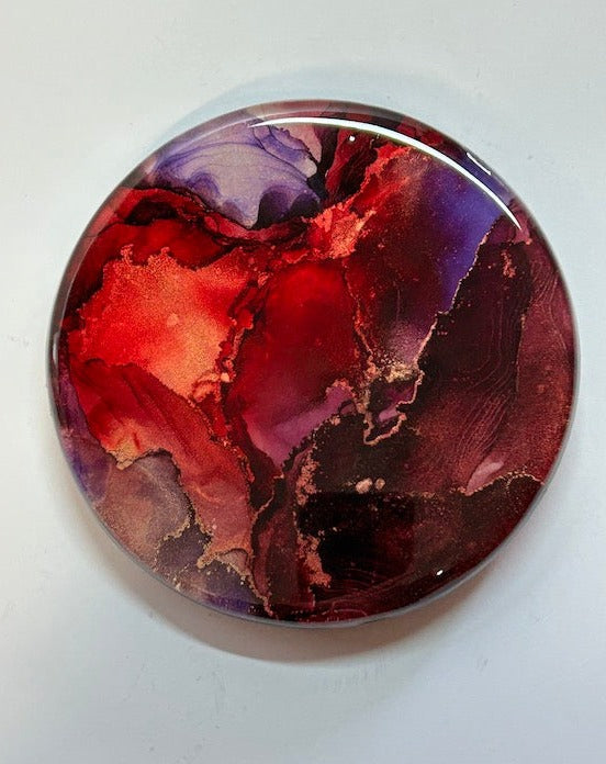 Interior abstract fluid art. Fluid tones of red, violet and maroon flow and overlap in this resin art painting. Copper details appear throughout. 6” circular wall art.