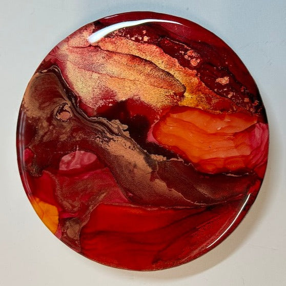 ‘Enfold,’ a circular abstract, resin topped wall painting full of fiery reds, gold and copper. 6” diameter. Fluid art painting for the home by Inkandescent Arts. Original resin red abstract  ink wall art expression.  WALL ART. ART FOR THE HOME.