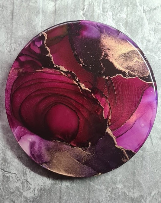 Wall decor full of impact and deep colours. Expressive life-force themed, original artwork features reds, hints of aubergine, slips of hot pink and metallic ink. Topped with resin, fractures and dark spirals intersect across the span of this 10” abstract circular wall art. By Inkandescent Arts. Original red resin abstract ink painting. Modern round wall art.