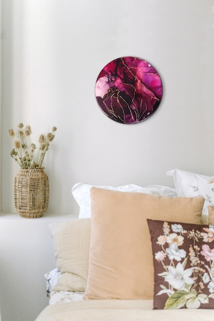 A colourful abstract painting displayed as bedroom art on a wall above pillows and cushions. A round symbolic painting of depth and colour representing death and life by Inkandescent Arts.