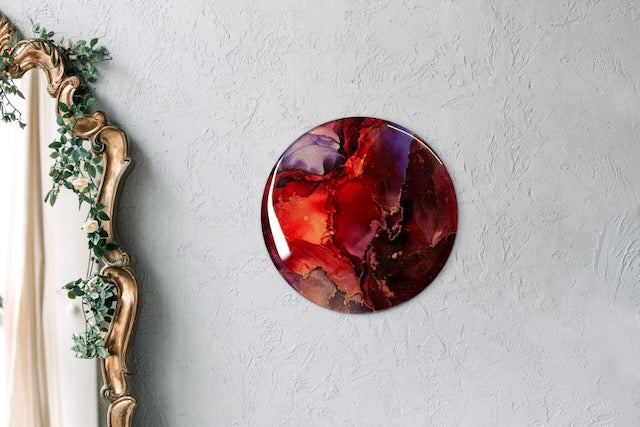 Round abstract painting on a wall next to a mirror. Maroon, red, purple and copper art that portrays endings and beginnings before we are reborn.  Transformation symbolism based on the arcana death card meaning and Phoenix rising by inkandescent Arts. 