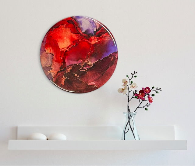 Small round artwork of lilac purple and maroon, adorns a wall above a shelf, vase and flowers. This abstract wall art is a symbol of resilience. Phoenix rising and death card inspired artwork by Inkandescent Arts.