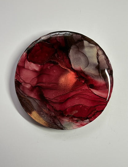 Round wall art featuring red and copper; symbolic abstract art that speaks of rebirth and transformation, renewal and resilience through the colours of the painting.