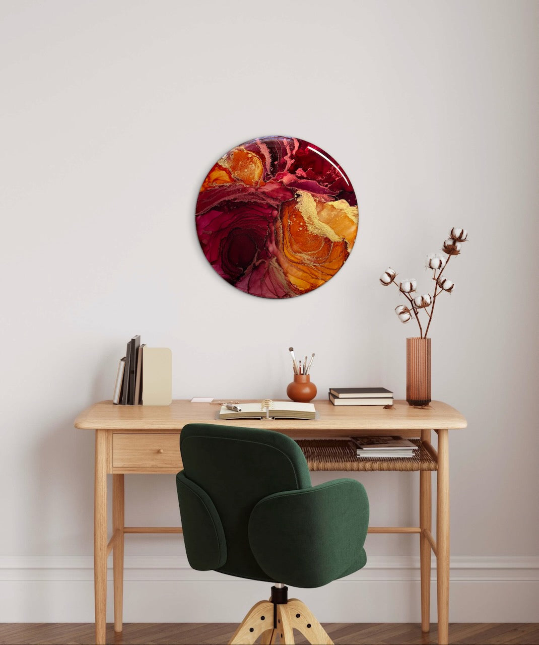 Circular wall art decor of orange red and gold on an neutral coloured office wall above a wooden desk with a green chair. Abstract phoenix rising; rebirth symbolism in art representing courage, rebirth and transformation. 