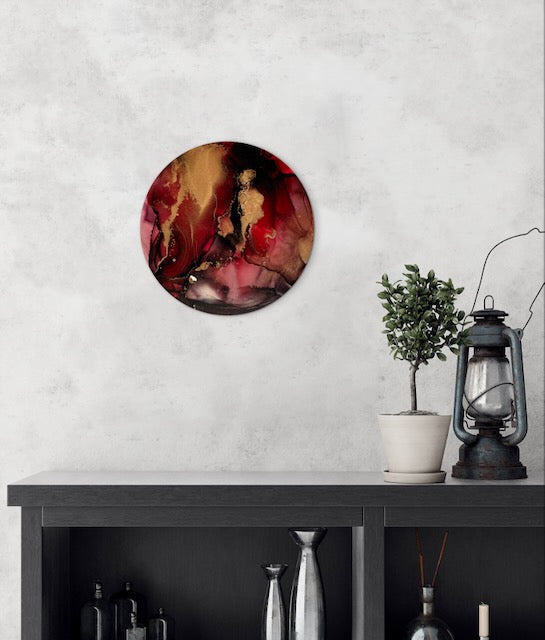 Round modern wall art, living room in red, rich gold and carbon black, hung above a cabinet.  A collision of bold and ethereal collide in this abstract artwork, influenced by the phoenix of myth and death tarot meaning. Life and death symbol by Inkandescent Arts.