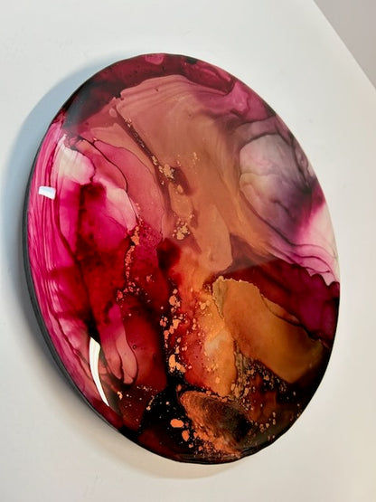 Round art displayed angled on a white wall showing a closer view of black, fuchsia and copper before fading to magenta. Exploring themes of the tarot death card and the phoenix, and a symbol of change by Inkandescent Arts.