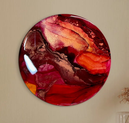 A front view of a round abstract painting displayed on a wall in sun and blood red colours. A death and rebirth symbol representing the cycle of change, and reigniting our inner fire - by Inkandescent Arts.