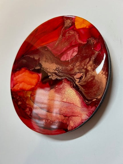 Burgundy and orange red colours bleed across this circular painting in a small, eye catching display. 
