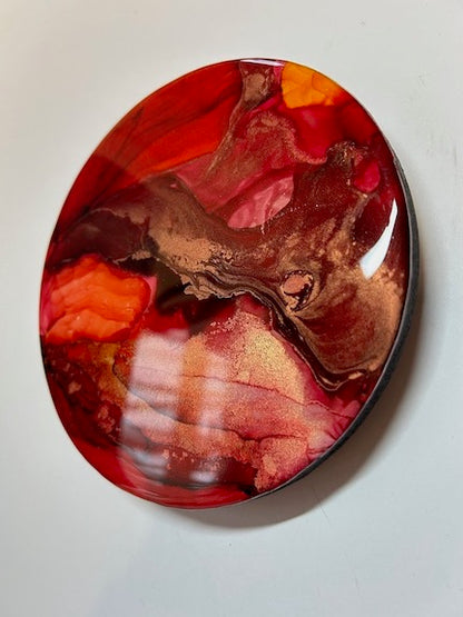 Burgundy and orange red colours bleed across this circular painting in a small, eye catching display. 
