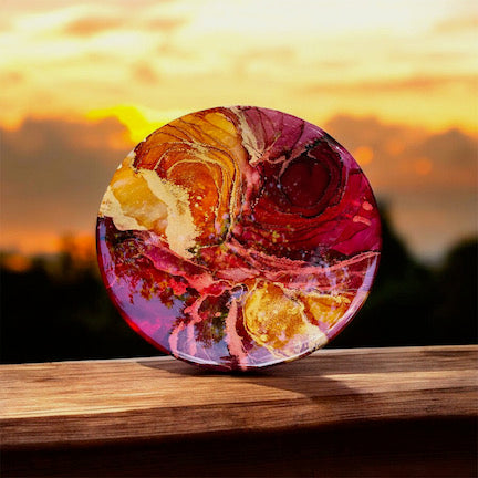A contemporary painting in a round design. Original art featuring ripples, gold details and warm, fluid colours of orange and red. A 10” original painting, topped with resin.
