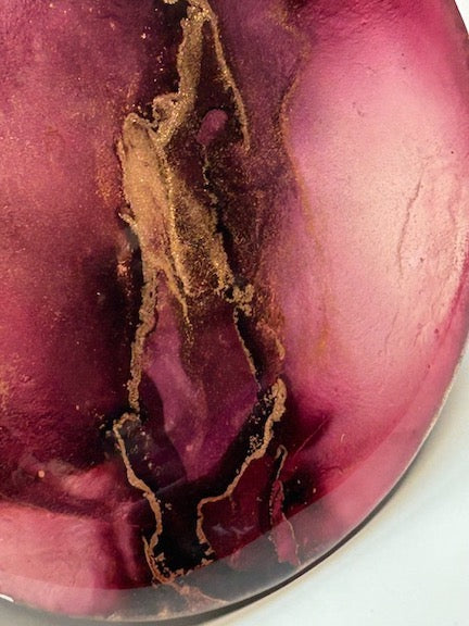 Circular art, wall decor crafted in inks and topped in multiple layers of resin, ‘Ignite’ is an original abstract, fluid art painting comprised of burgundy, brass and black. 
