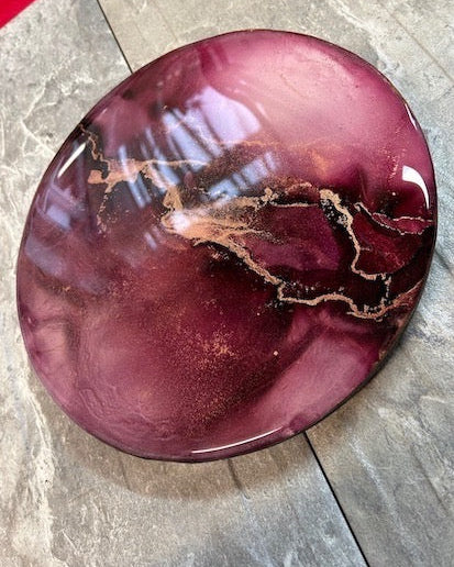 Interior art based on the mythical Phoenix, an abstract expression featuring maroon red topped with layers of resin. Fractures of brass intersect across the span of this 10” circular abstract painting. 
