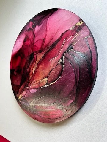 Circular abstract painting with burgundy, red, and pink colours with added 23k gold leaf, on a white background. Phoenix rising symbolism and taking a positive attitude to overcoming adversity.