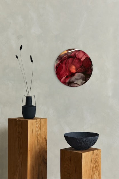 Round wall art of maroon, grey and gold hangs on a wall over plinths and ornaments. Phoenix symbolism that speaks of overcoming adversity. This symbol of power represents moving on after a stage of your life is complete - to the next stage allowing for personal growth. Artwork by Inkandescent Arts.