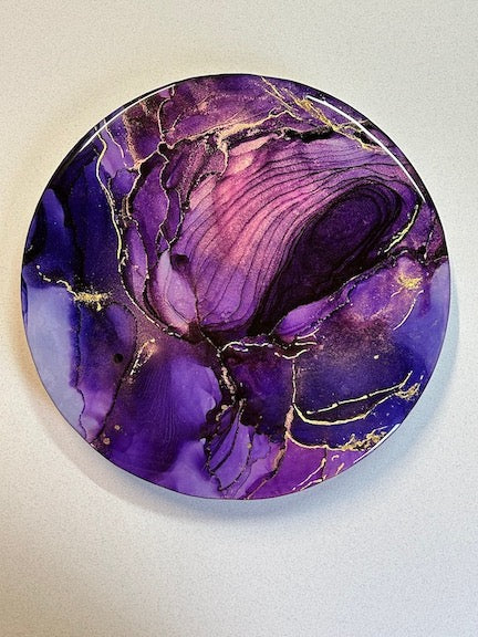 A circular abstract vision with a wildflower palette of violet and lavender. Gold metallic webs throughout the painting and highlights of 23 carat gold add to the clashing turbulence of this painting. Multiple resin coats give it that reflective surface - like portals of water and light -  adding to the magic of this piece.
A beautiful piece of elegance for your walls. By Inkandescent Arts.
