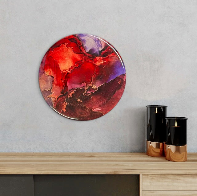 A circular painting adorns a wall above a mantle with candles. A rebirth symbol based on the phoenix rising from the ashes in original abstract wall art in burgundy, purple and blood red by Inkandescent Arts.