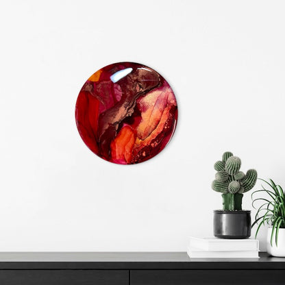 A circular red and gold room decoration on a wall with cactus plants on a sideboard beneath.  An abstract symbolism of rebirth and emerging from adversity.