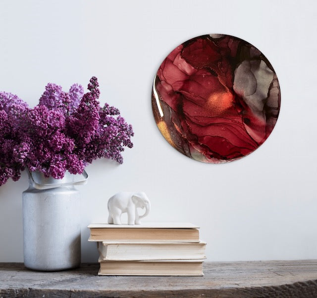 Maroon and brass artwork; round art on a living room wall over a mantle with decorative ornaments. A painting for interiors representing resolve and inner strength, clarity and vision as we rise transformed from the ashes.