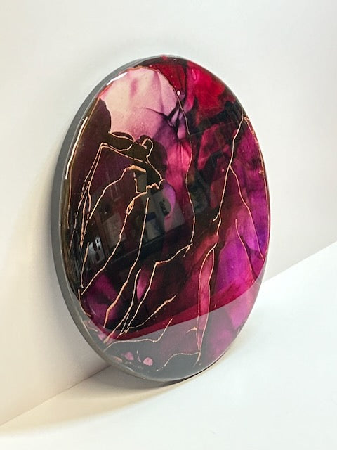 Strength and courage symbol in a round abstract painting of maroon, purple, deep red and copper displayed at an angle. This round artwork explores the connection between the death card meaning and the phoenix rising symbolism through colour, depth and emotion - by Inkandescdent Arts.
