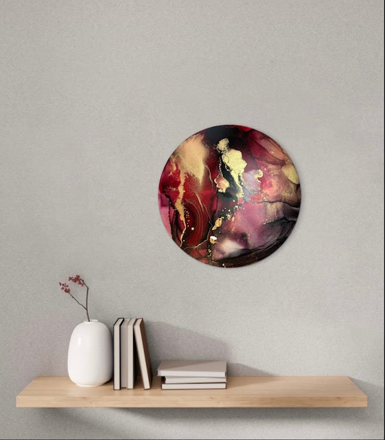 Transformative art, symbolic of healing, decorates a wall over a shelf in an interior. A round intuitively painted original abstract artwork for sale in uk, of 10 inches in black, red and gold. By Inkandescent Arts.